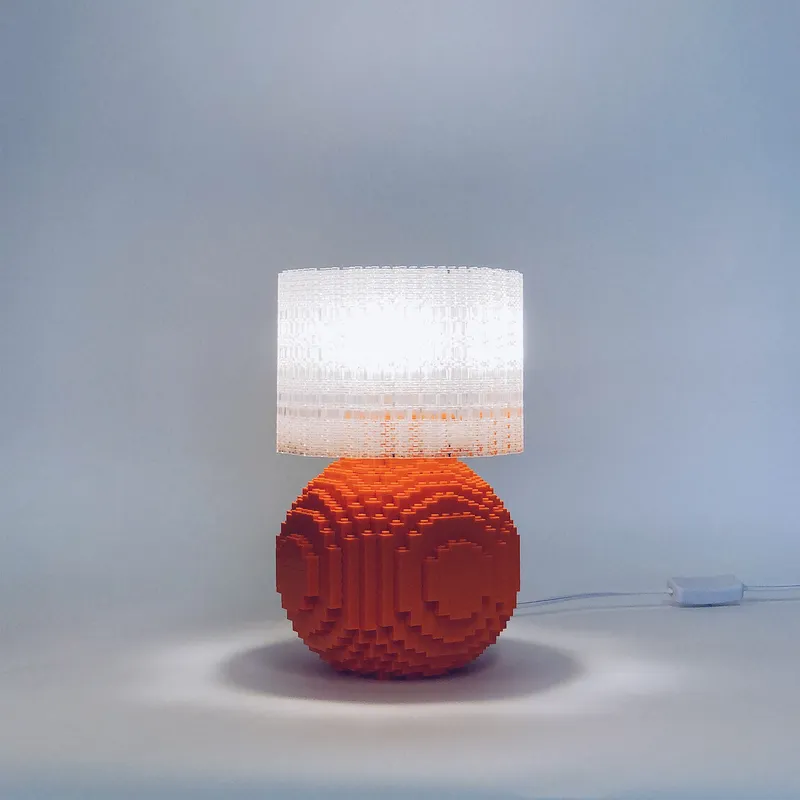 An orange Splash of Color lamp lit against a soft gray studio backdrop.