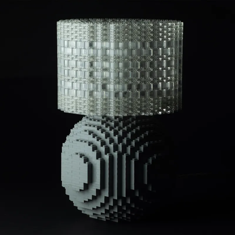 A gray Splash of Color lamp with a translucent brick shade on a black studio backdrop.
